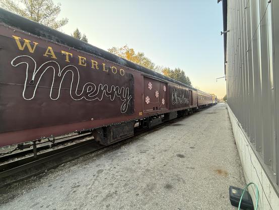 A maroon baggage car with “merry christmas” in lights on the side, in the middle of a train leading off into the distance